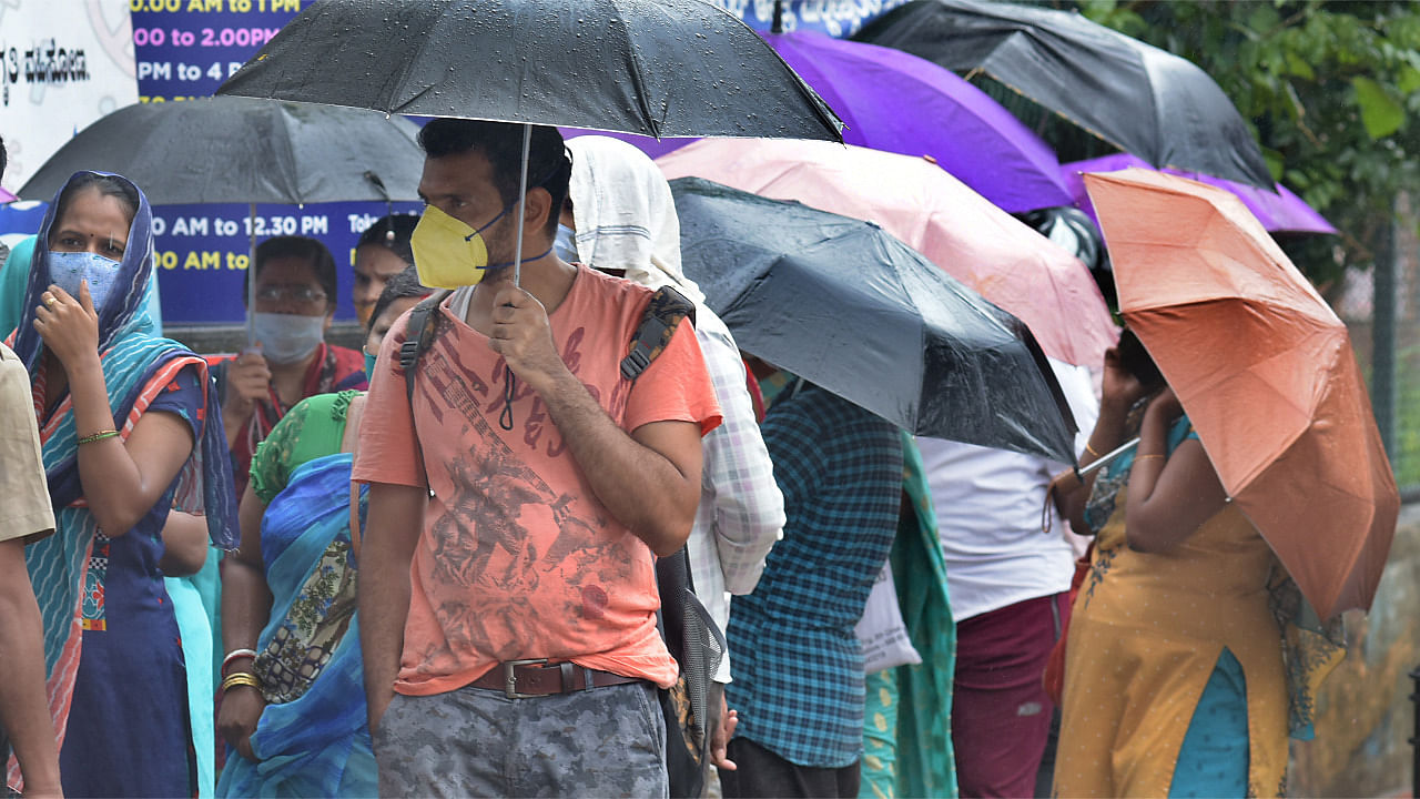People brace the rain waiting for their turn to get Covid vaccine at a vaccination centre by KC General in Malleswaram, Bengaluru. Credit: DH Photo/Pushkar V