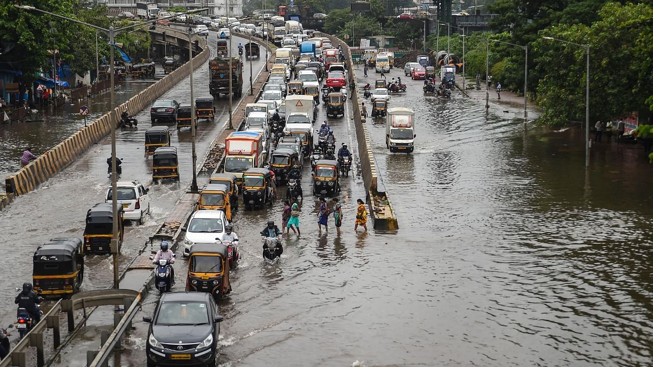 Commuters wade through a waterlogged street as heavy rain continues at Santacruz- Chembur Link Road, in Mumbai, Sunday, July 18, 2021. Credit: PTI Photo