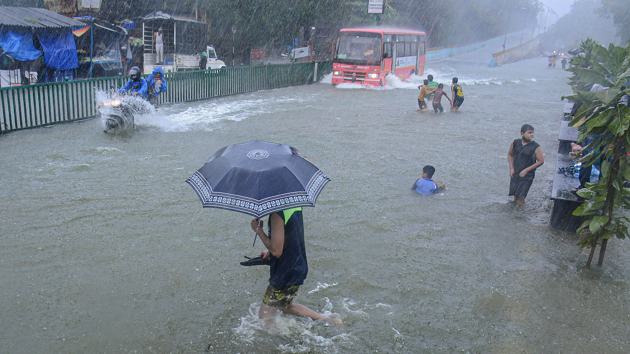 Commuters wade through a waterlogged road after the Masunda lake overflowing due to heavy rains in Thane. Credit: PTI Photo