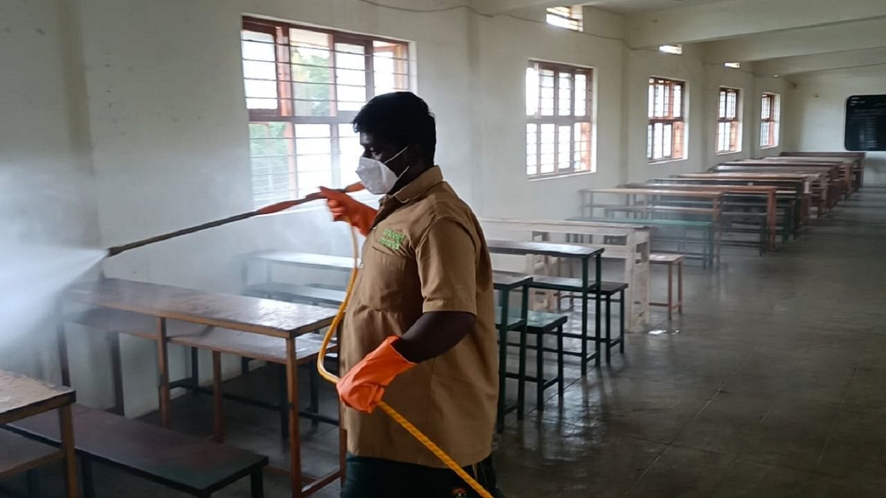 A worker sprays benches in a classroom with a disinfectant ahead of the SSLC exams in Chamarajanagar. Credit: DH Photo