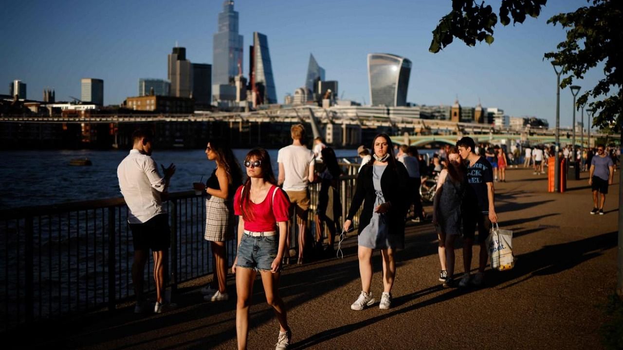 People enjoy the evening sunshine on Thames Embankment by the river Thames with the skyline of the City of London in the background in London. Credit: AFP Photo