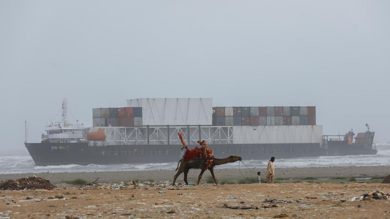 A man leads his camel as a cargo ship Heng Tong 77 is seen stranded near Sea View beach in Karachi