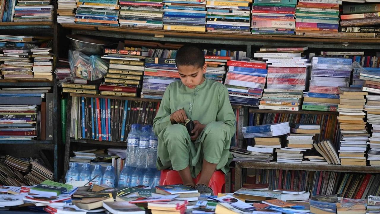 A child checks his wallet as he sits at a roadside bookshop at a market in Kabul. Credit: AFP Photo
