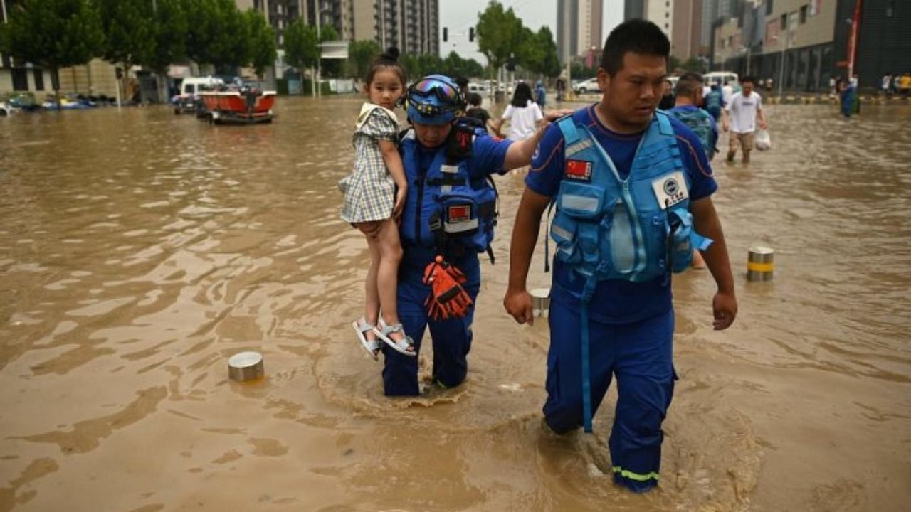 Members of rescue organization Bluesky rescue team carry a girl across a flooded street following a heavy rain in Zhengzhou, in China's Henan province on July 22, 2021. Credit: AFP Photo