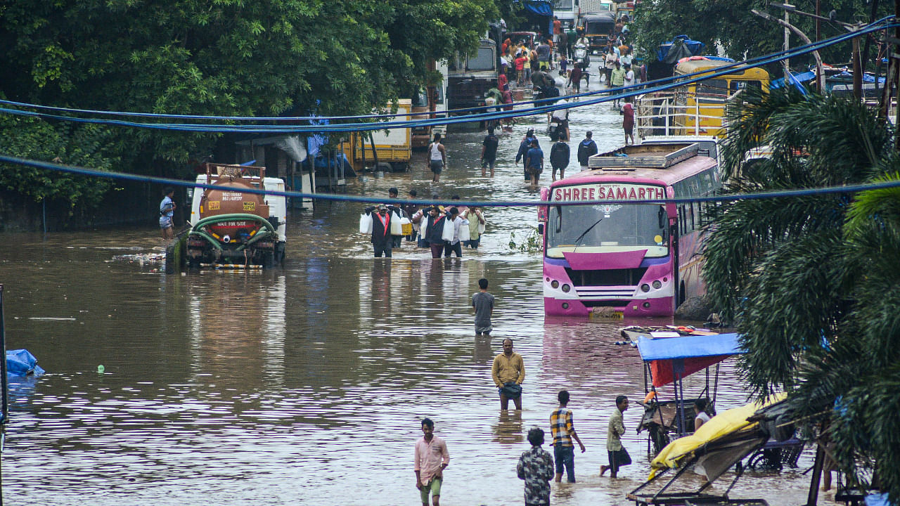 Commuters wade through a flooded road after heavy rain at Bhiwandi in Thane. Credit: PTI Photo