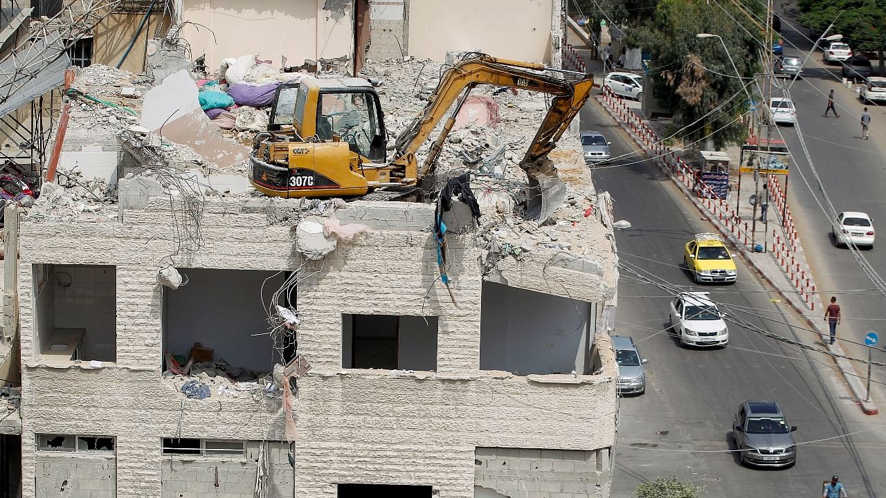 A machinery works to remove the debris atop a building damaged in Israeli air strikes during the fighting between Israel and Hamas, in Gaza City. Credit: Reuters photo