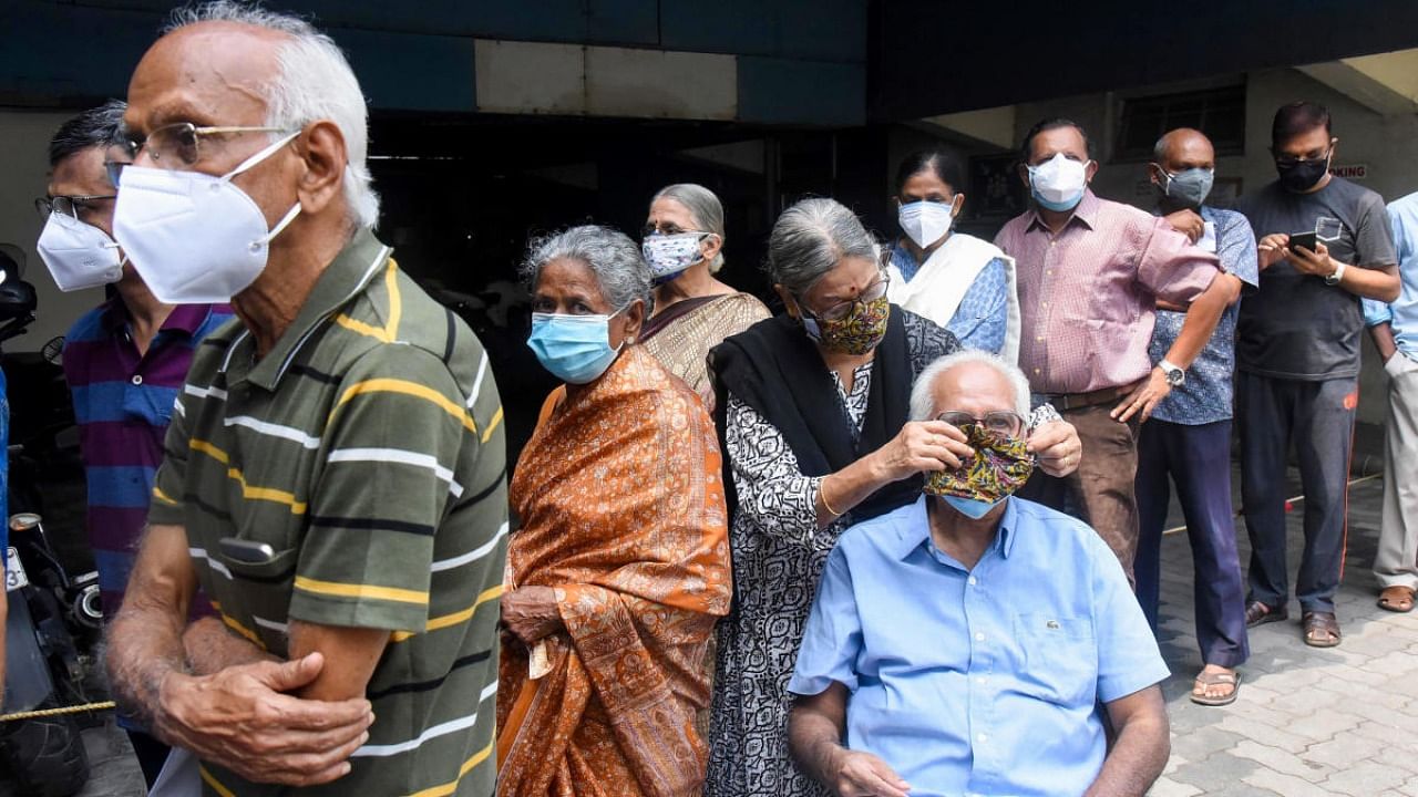 A woman puts a mask to her husband while waiting for vaccination against Covid-19, in Kochi, Saturday, May 8, 2021. Credit: PTI File Photo