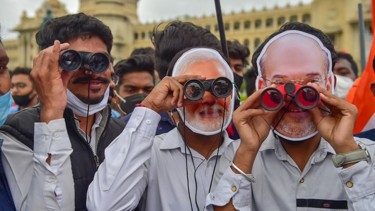 Congress workers wearing face masks of PM Modi and Home Minister Amit Shah, hold binoculars during their protest against the central government over an alleged surveillance operation using the Pegasus spyware, in Bengaluru. Credit: PTI Photo