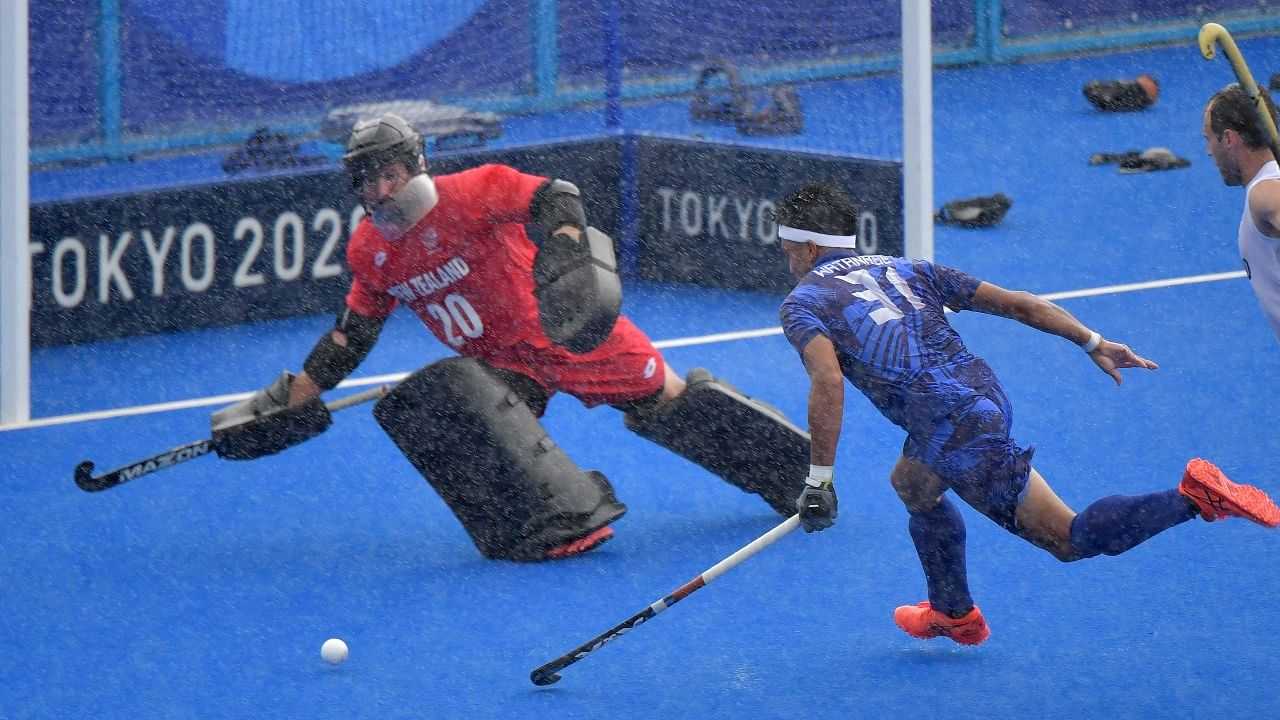 Japan's Kota Watanabe (C) and New Zealand's goalkeeper Leon Hayward (L) vie for the ball under heavy rain during their men's pool A match of the Tokyo 2020 Olympic Games field hockey competition, at the Oi Hockey Stadium in Tokyo. Credit: AFP Photo