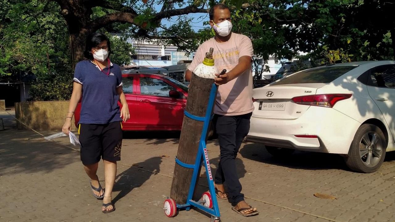 A couple walks with an oxygen cylinder for a Covid-19 coronavirus patient addmited at the Goa Medical College and Hospital (GMCH), where 26 people admitted in the hospital due to the coronavirus died on the early morning, in Panjim. Credit: PTI File Photo
