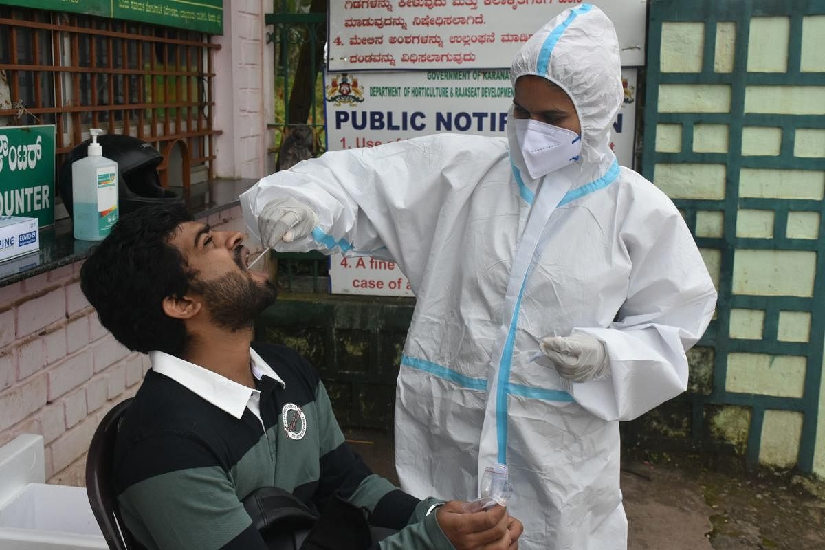 A healthcare worker collects a swab sample from a tourist at Raja Seat in Madikeri.