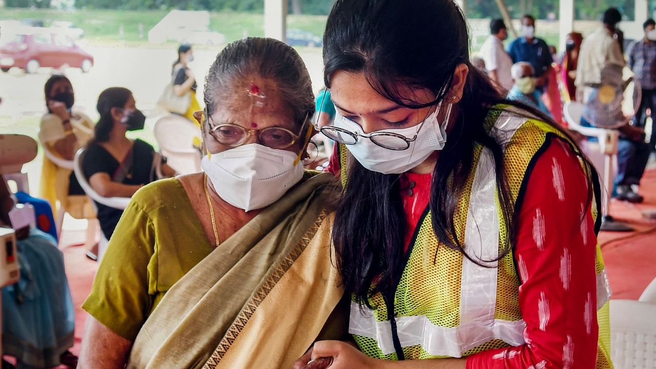 A health worker escorts an elderly woman to receive a dose of Covid vaccine in Kerala. Credit: PTI File Photo