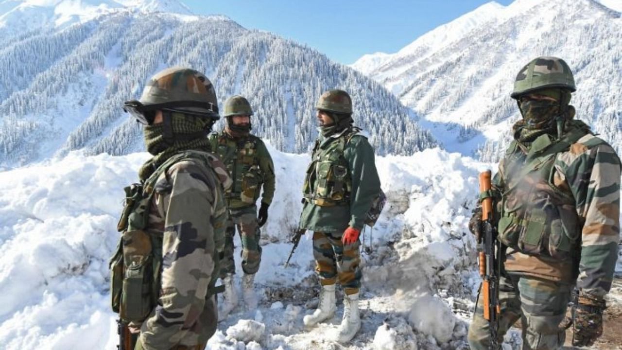 Indian army soldiers stand on a snow-covered road near Zojila mountain pass that connects Srinagar to the union territory of Ladakh, bordering China on February 28, 2021. Credit: AFP Photo