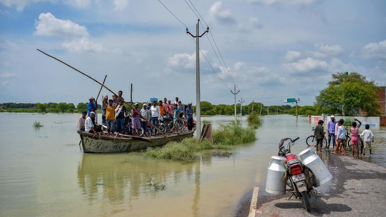 People use a boat to cross a waterlogged area after rising water level in river Ganges caused flooding at Badara Sanuti village, near Allahabad on August 6, 2021. Credit: AFP Photo
