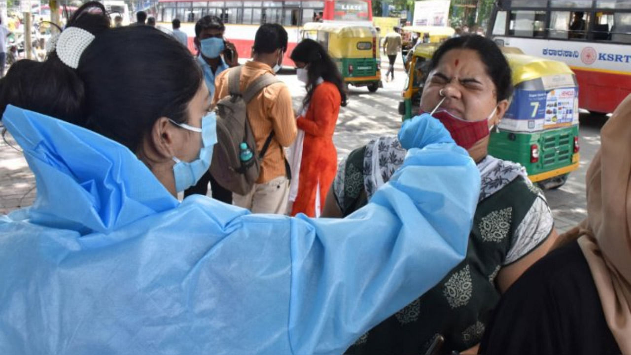A healthcare worker collects the swab samples of a passenger for Covid testing at the KSR Bengaluru railway station on Saturday. Credit: DH Photo/Janardhan B K