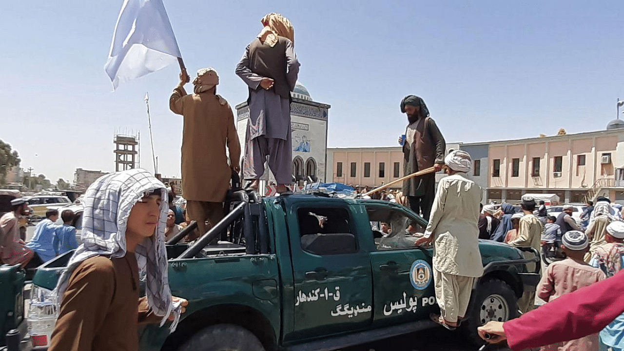 Taliban fighters stand over a damaged police vehicle along the roadside in Kandahar. Credit: AFP Photo