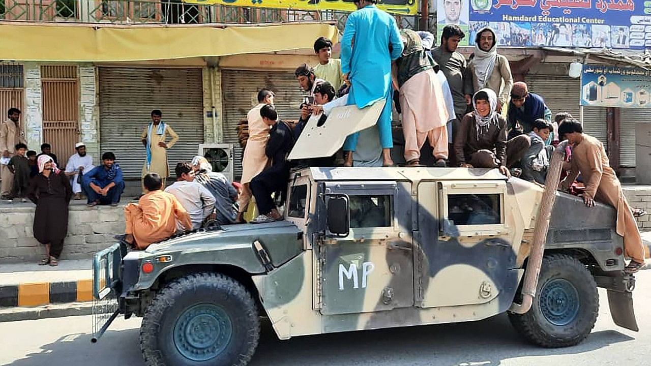 Taliban fighters and local residents sit over an Afghan National Army (ANA) humvee vehicle. Credit: AFP Photo