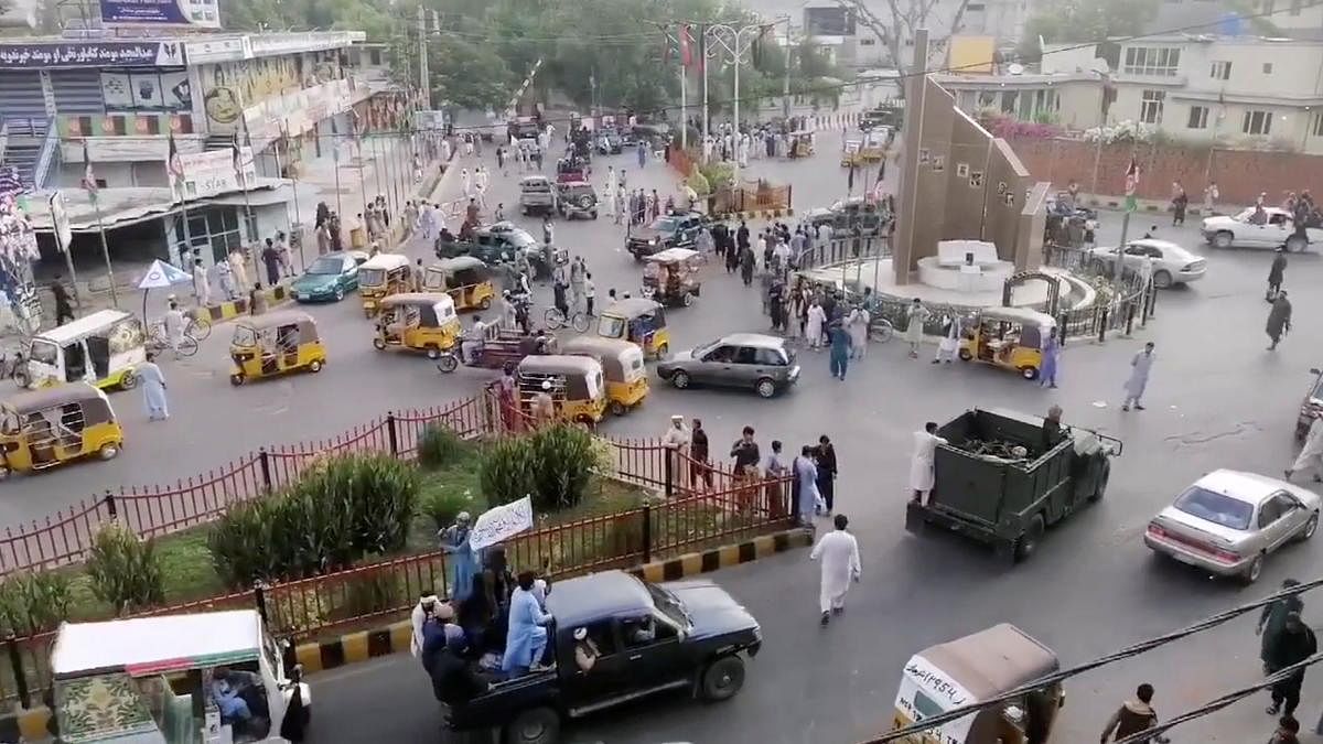 Taliban militants waving a Taliban flag on the back of a pickup truck drive past a crowded street at Pashtunistan Square area in Jalalabad, Afghanistan in this still image taken from social media video uploaded on August 15, 2021. Credit: Reuters Photo