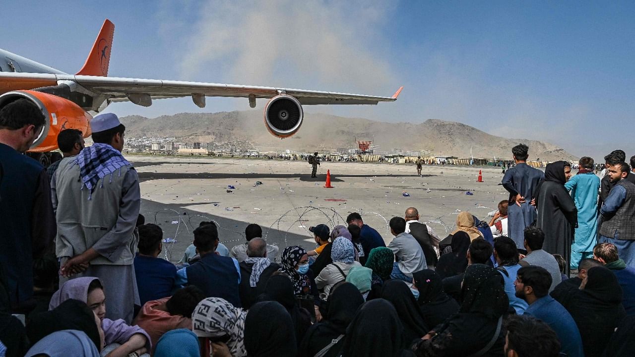 Afghan people sit as they wait to leave the Kabul airport. Credit: AFP Photo