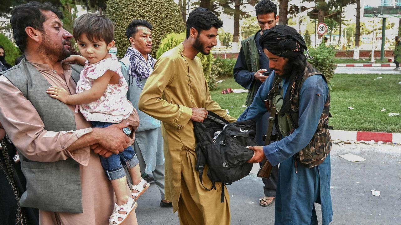 A Taliban fighter (R) searches the bags of people coming out of the Kabul airport in Kabul. Credit: AFP Photo