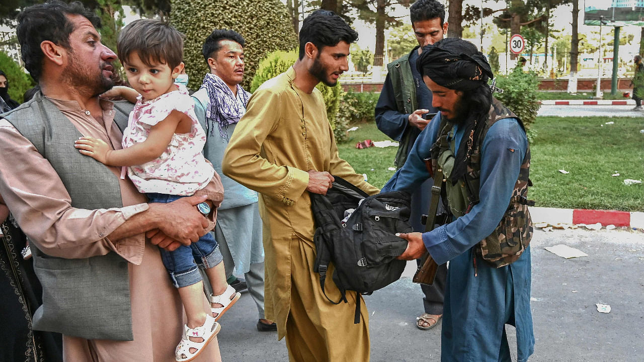 A Taliban fighter (R) searches the bags of people coming out of the Kabul airport in Kabul. Credit: AFP Photo