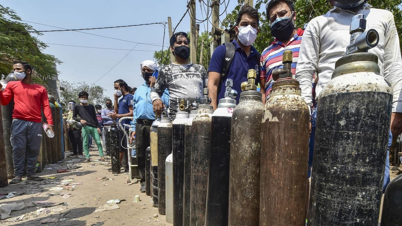 Family members of Covid-19 patients wait outside an oxygen-filling centre to refill their empty cylinders, as demand for the gas rises due to a spike in coronavirus cases, at Naraina in New Delhi. Credit: PTI Photo