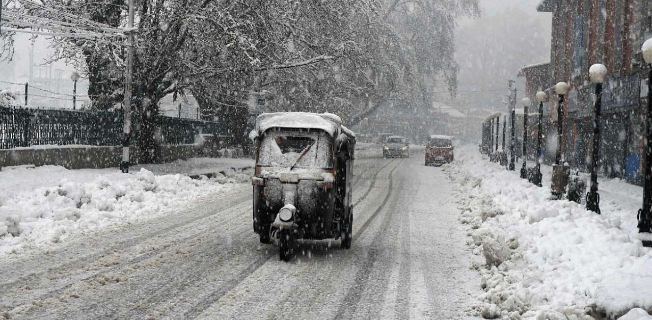 An auto-rickshaw moves slowly on a snow-covered road during heavy snowfall, in Srinagar, Tuesday. Credit: PTI Photo