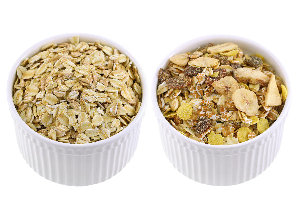 White cups full of raw rolled oats next to Packaged muesli with various dried fruit and seeds.