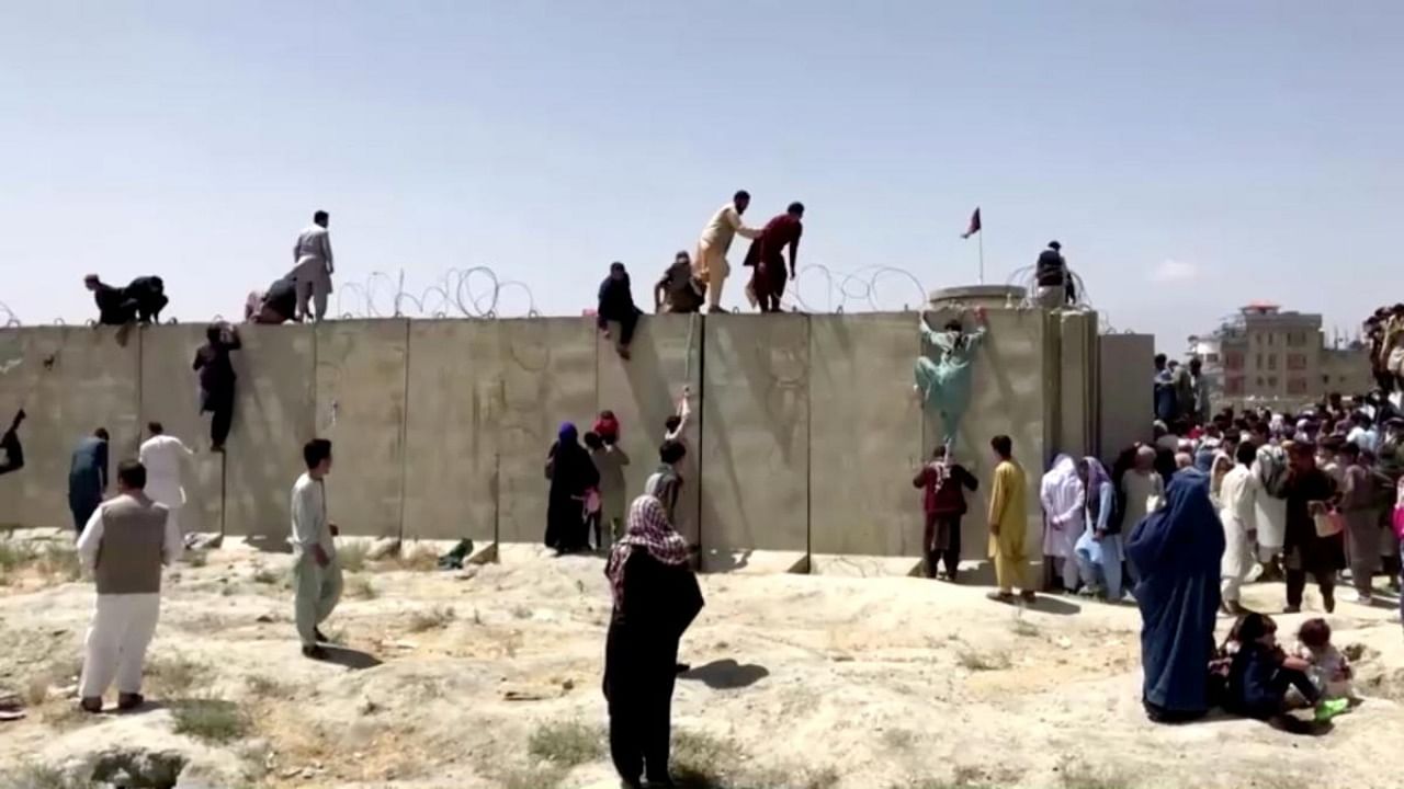 People climb a barbed wire wall to enter the airport in Kabul, Afghanistan August 16, 2021, in this still image taken from a video. Credit: Reuters photo