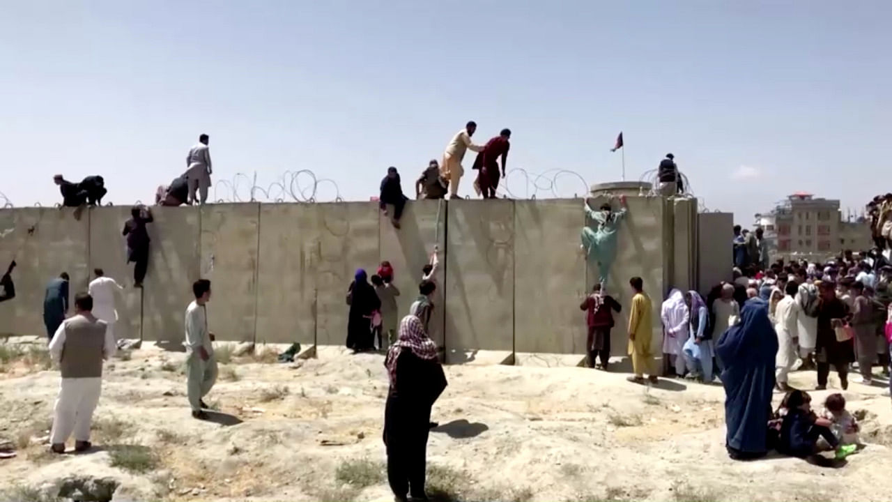 People climb a barbed wire wall to enter the airport in Kabul. Credit: Reuters Photo