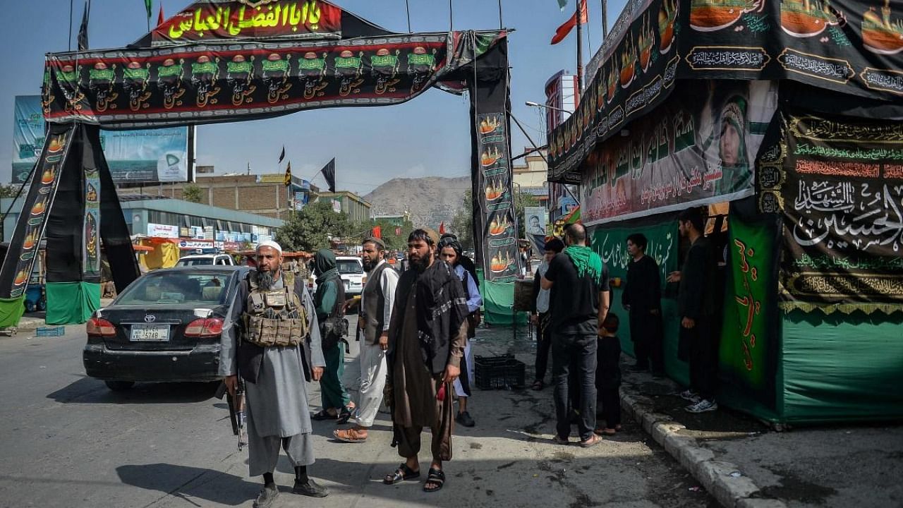 Taliban fighters stand guard near a makeshift tent where the Shiite Muslims distribute sherbet to people during the Ashura procession which is held to mark the death of Imam Hussein, the grandson of Prophet Mohammad, along a road in Kabul on August 19, 2021, amid the Taliban's military takeover of Afghanistan. Credit: AFP Photo