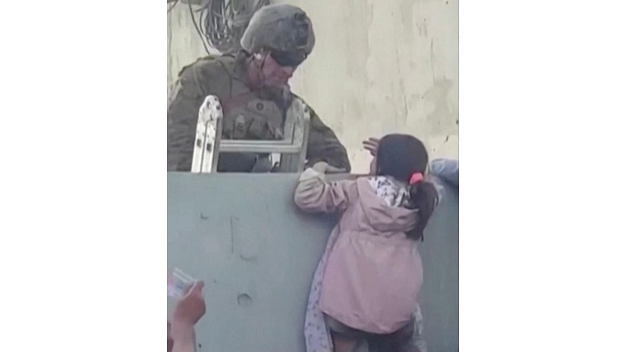 US soldier stands guard while a girl tries to climb the wall as crowds gather near the wall at Kabul airport, Afghanistan August 17, 2021. Credit: Rise to Peace via Reuters Photo