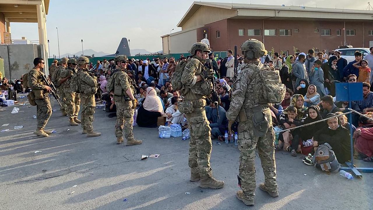 US soldiers stand guard as Afghan people wait to board a US military aircraft to leave Afghanistan, at the military airport in Kabul. Credit: AFP Photo