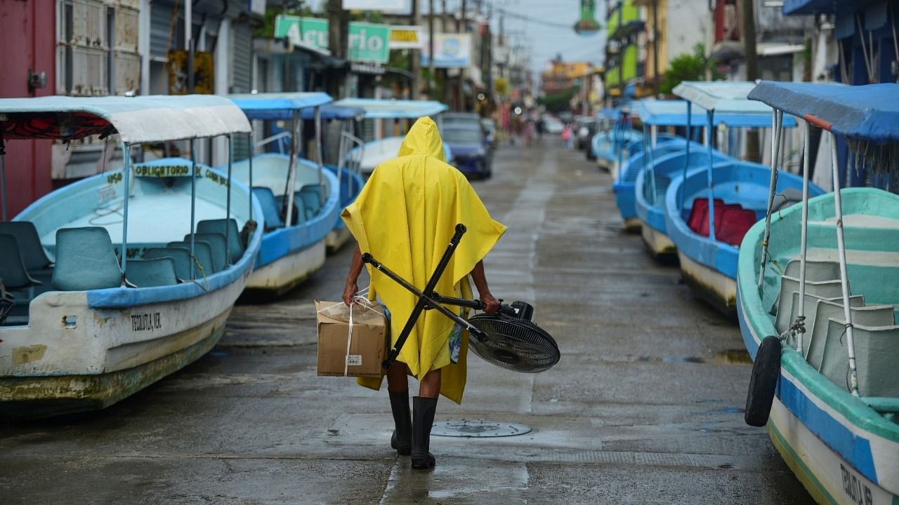 A man carries a fan and a box while walking past tourist boats that were moved from the water for safety as Hurricane Grace gathered more strength before reaching land. Credit: Reuters Photo