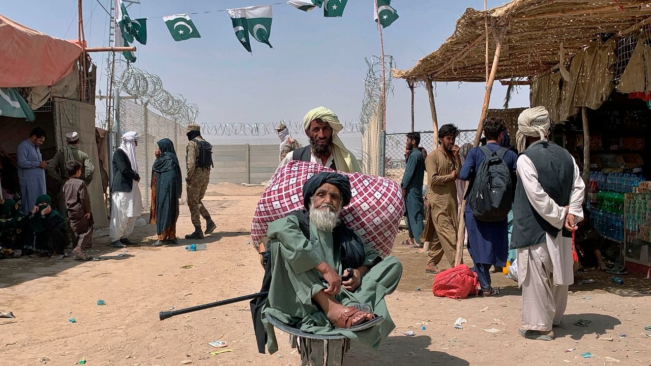 A porter pushes a wheelbarrow carrying an elderly Afghan man as he enters into Pakistan through a border crossing point. Credit: AP/PTI Photo