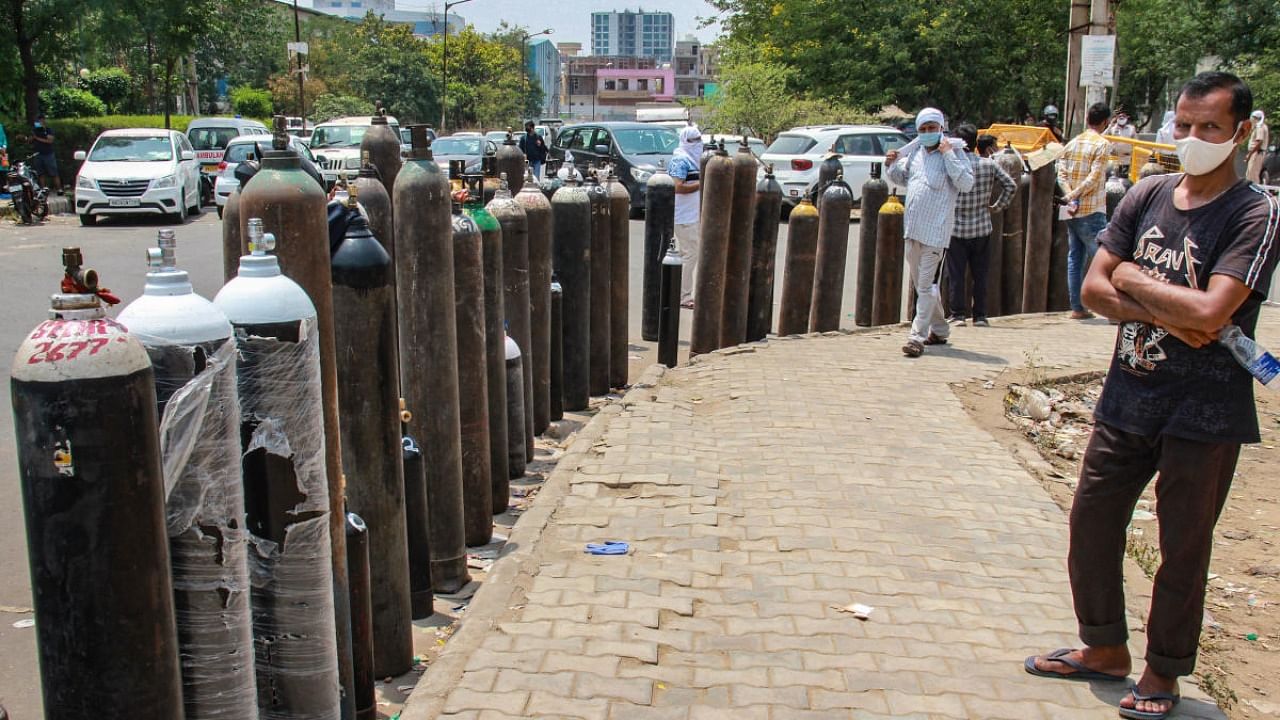 Relatives of Covid-19 patients wait to fill empty cylinders at an oxygen filling center, as demand for the gas rises due to spike in coronavirus cases, at IMT Manesar near Gurugram. Credit: PTI File Photo