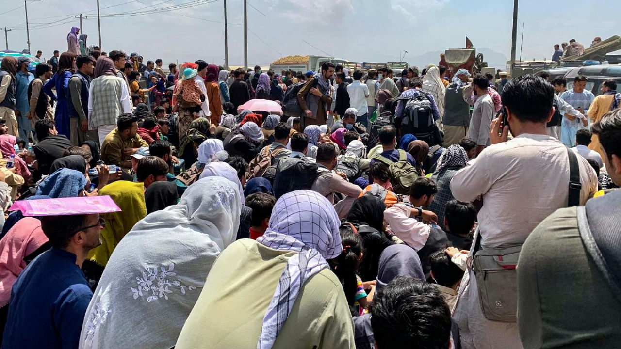 Afghan people gather along a road as they wait to board a US military aircraft to leave the country, at a military airport in Kabul. Credit: AFP Photo