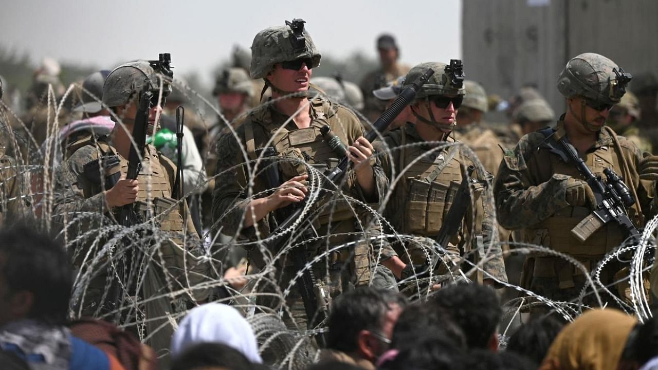 US soldiers stand guard behind barbed wire as Afghans sit on a roadside near the military part of the airport in Kabul. Credit: AFP Photo