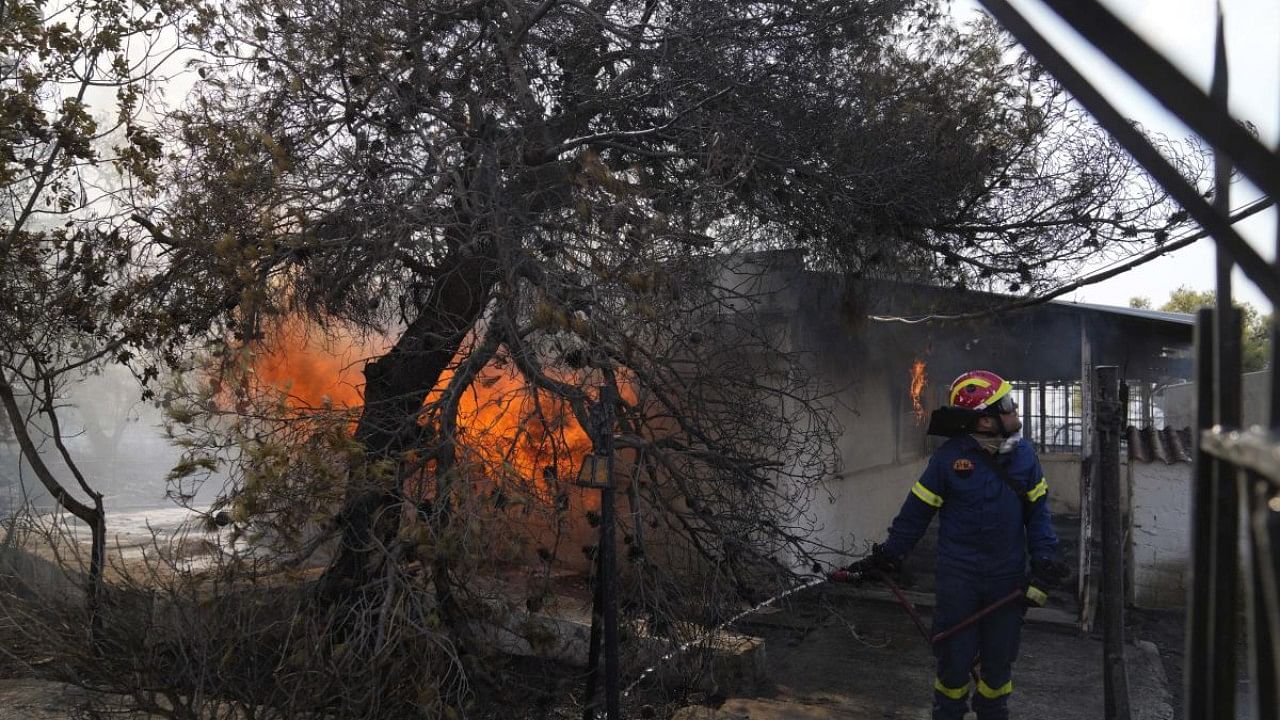 A firefighter extinguish the fire to a house during a wildfire in Thea area some 60 kilometers northwest of Athens. Credit: AP Photo