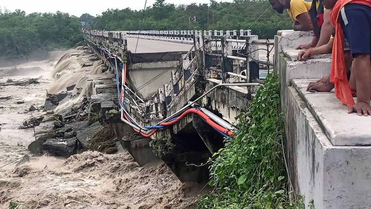 People look at the Rani Pokhri bridge on the Dehradun Rishikesh highway that collapsed due to heavy rains, near Dehradun. Credit: PTI Photo