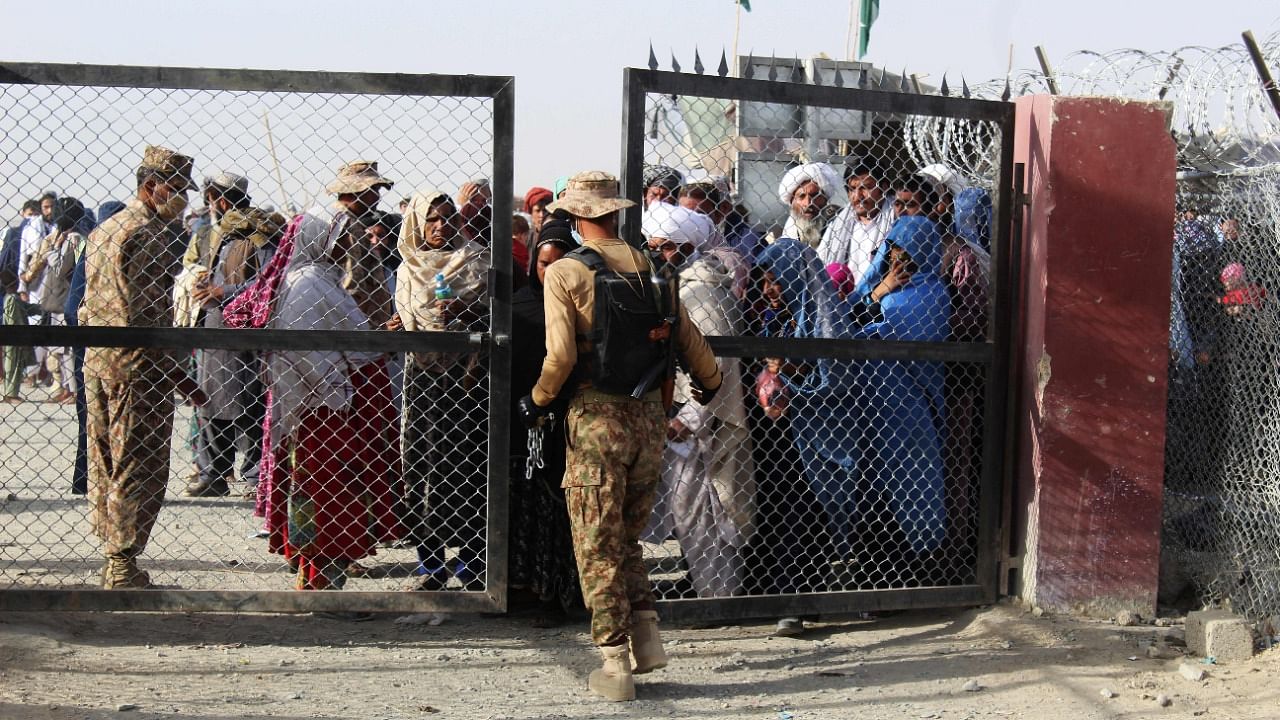 A Pakistani soldier holds a gate as Afghan and Pakistani people wait to enter Afghanistan. Credit: AFP Photo