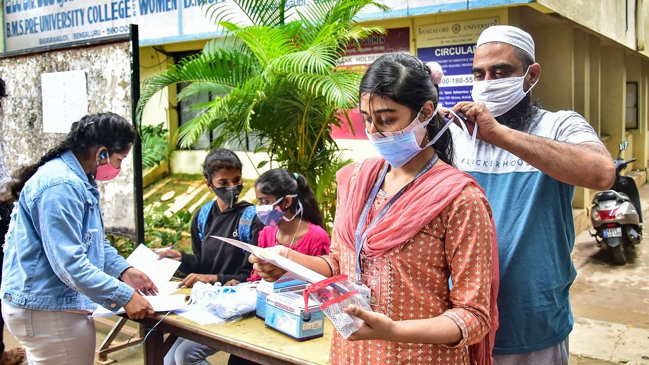 A volunteer helps a student to wear a face mask before she appears for the Common Entrance Examination (CET), at a college in Bengaluru, Saturday. Credit: PTI Photo