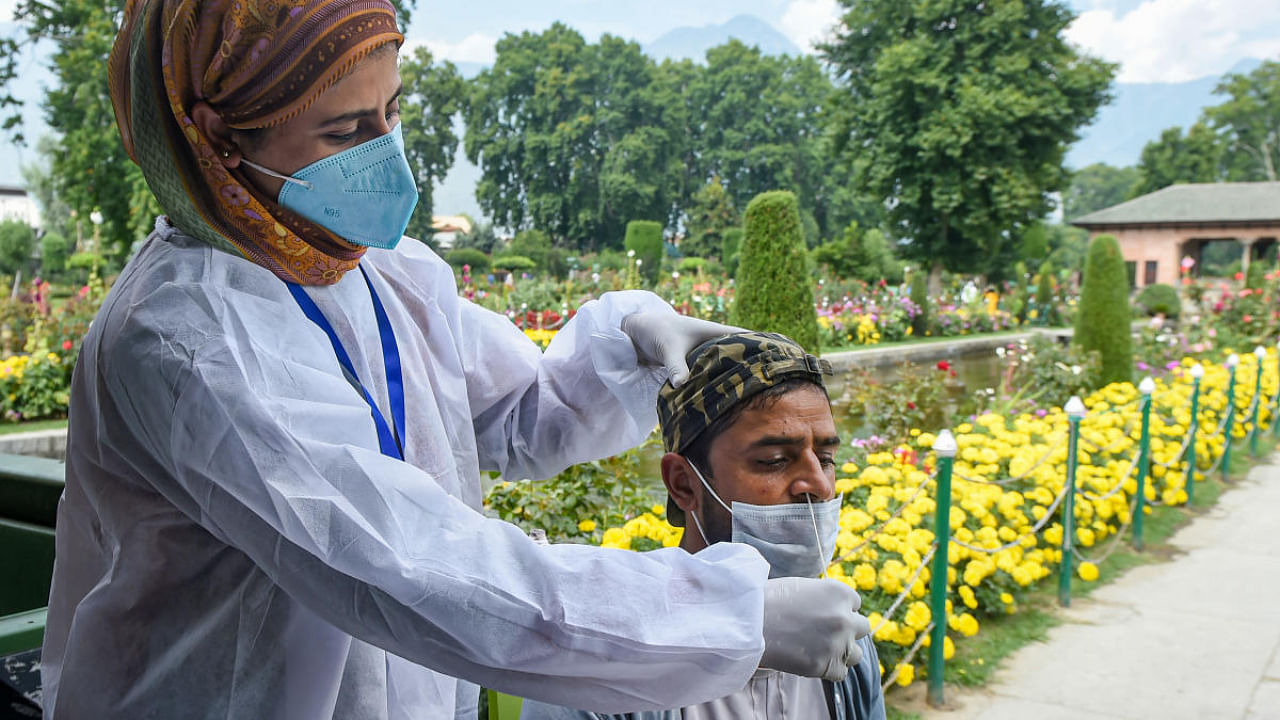 A medical employee takes swab sample of a visitor for Covid-19 rapid antigen test, before allowing him entry inside Mughal Garden Shalimar, in Srinagar. Credit: PTI Photo
