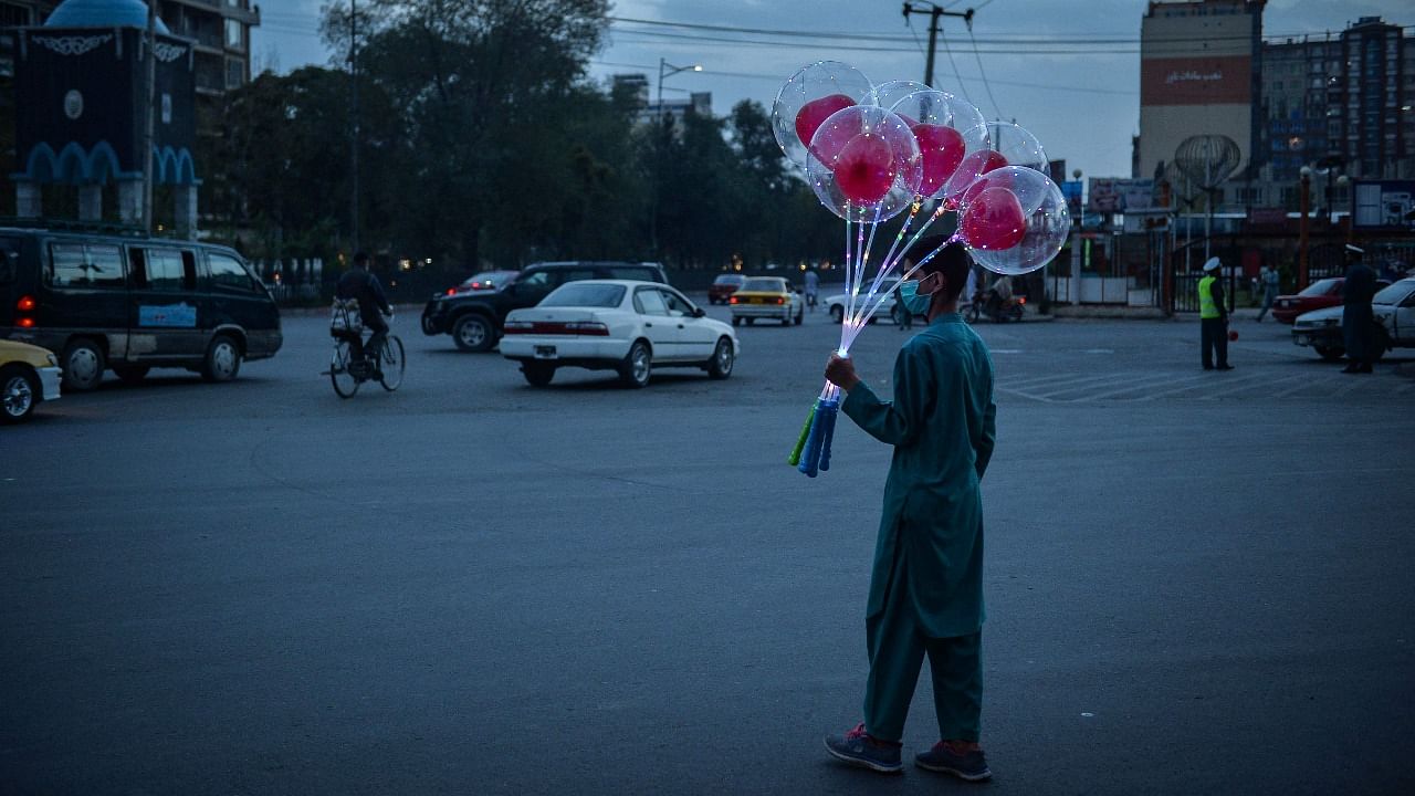 An Afghan boy stands along a road holding a bunch of balloons to sell in Kabul on August 30, 2021. Credit: AFP Photo