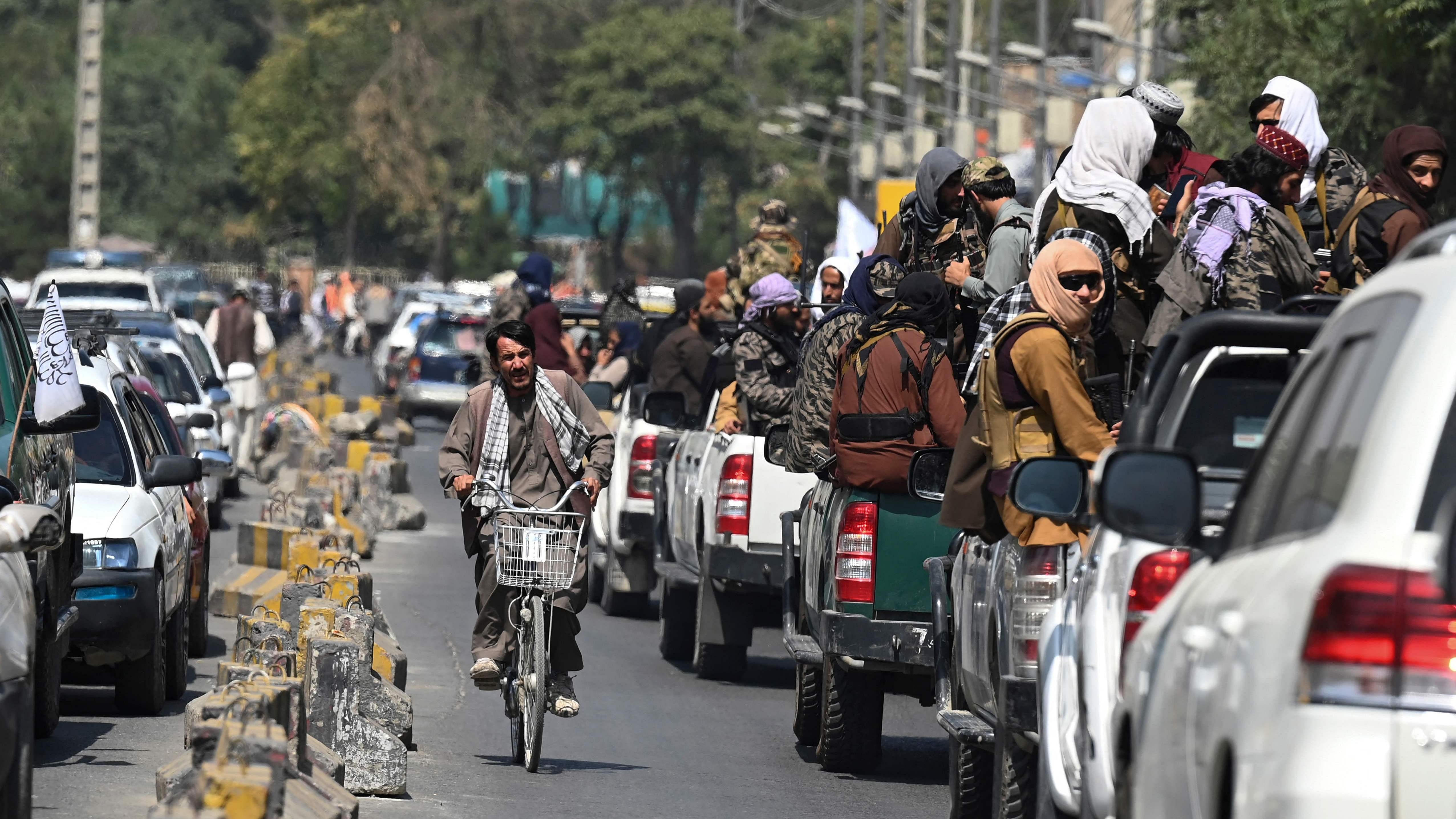 A man on his bicycle rides past a convoy of Taliban fighters patrolling along a street in Kabul. Credit: AFP Photo