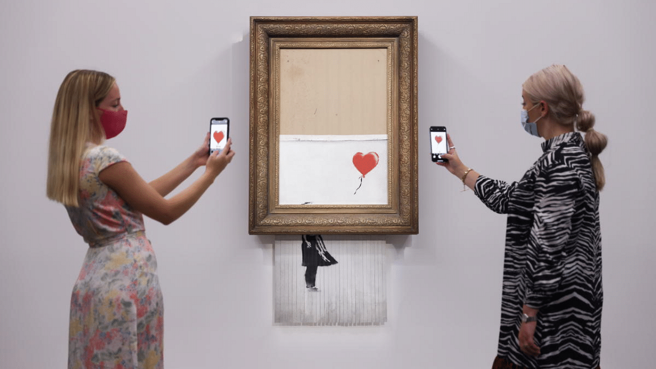 A gallery assistant poses by 'Love is in the Bin', an artwork by Banksy, which will be for sale in an auction, at Sotheby's in London, Britain. Credit: Reuters Photo