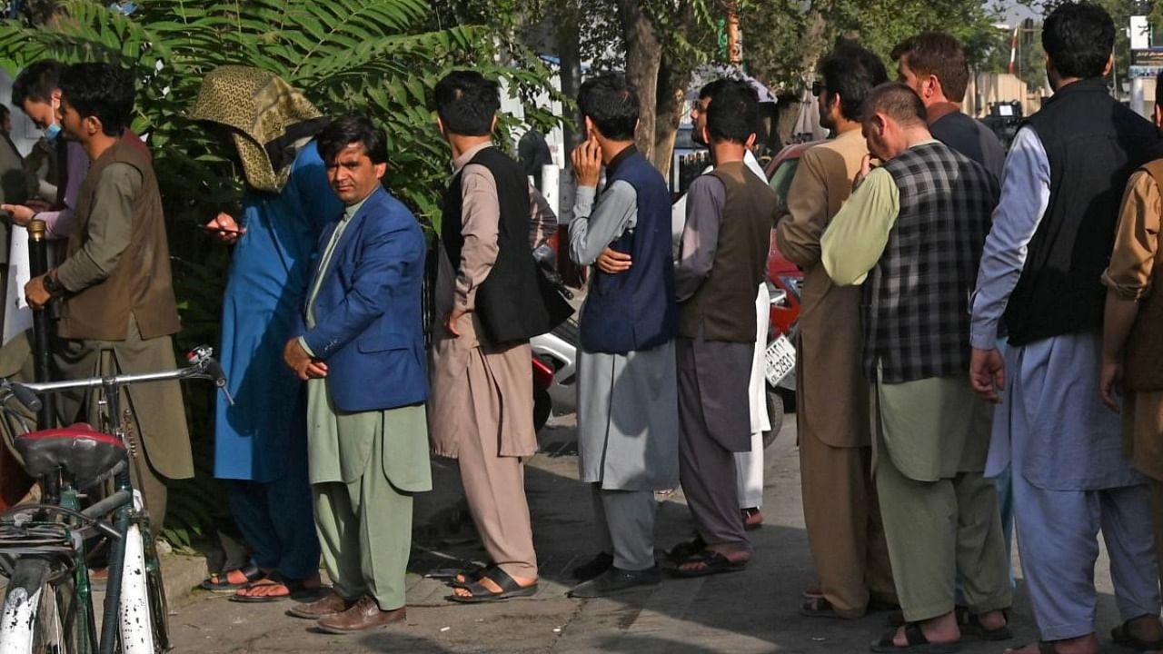 Afghan people stand in a queue as they wait for their turn to collect money from an ATM in front of a bank along a roadside in Kabul. Credit: AFP Photo