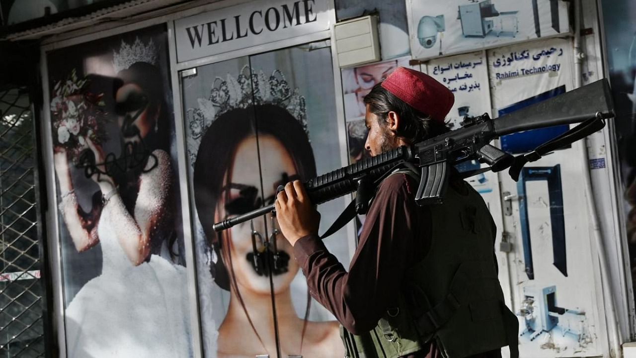 A Taliban fighter walks past a beauty saloon with images of women defaced using a spray paint in Shar-e-Naw in Kabul. Credit: AFP Photo