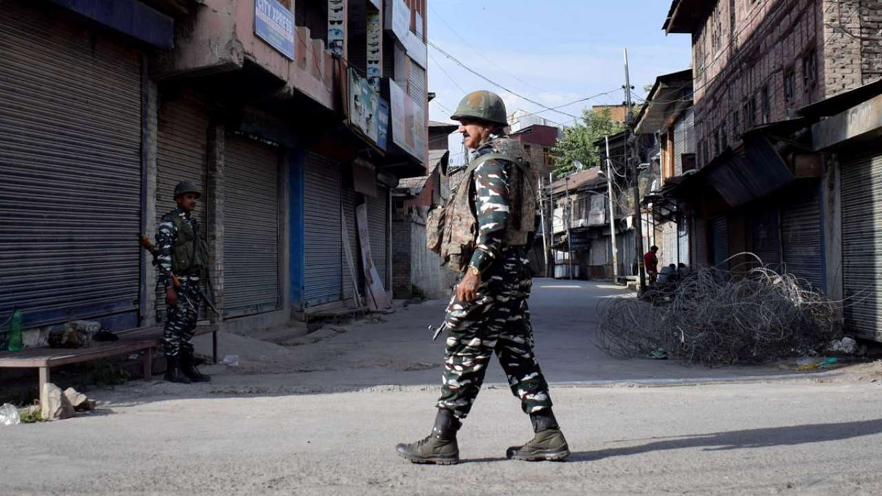 Security forces personnel stand guard in front of closed shops during restrictions imposed in Srinagar. Credit: Reuters Photo