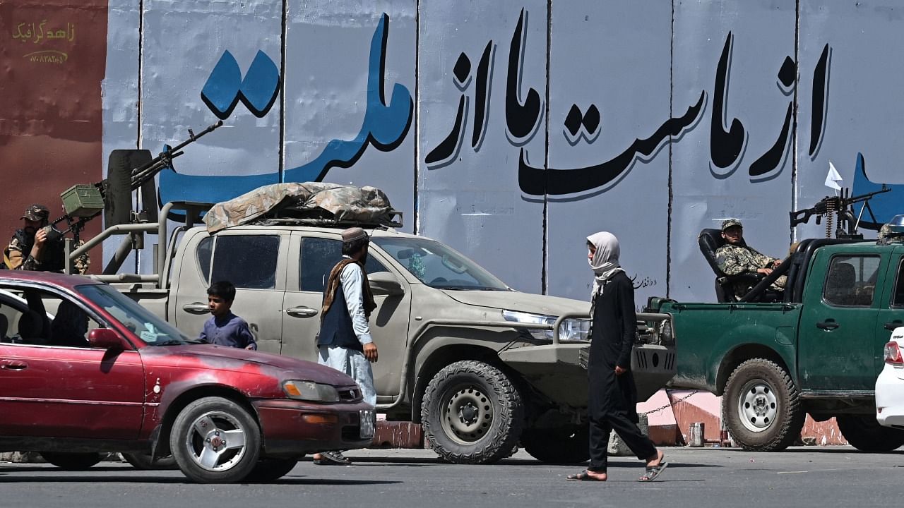 Commuters move past Taliban fighters sitting in their vehicles along a street in Kabul. Credit: AFP Photo